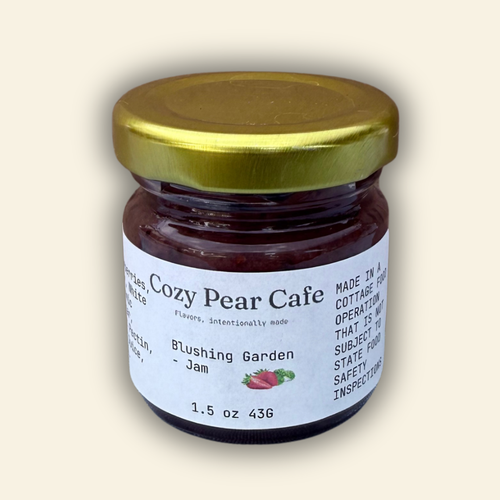 A jar of Cozy Pear Cafe Blushing Garden - Jam, featuring a white label and a metallic gold lid, set against a solid cream-colored background.