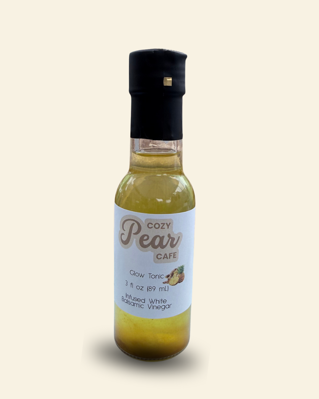 A bottle of Cozy Pear Cafe Glow Tonic, made from distilled white balsamic vinegar, featuring a white label and a black cap, set against a solid cream background.