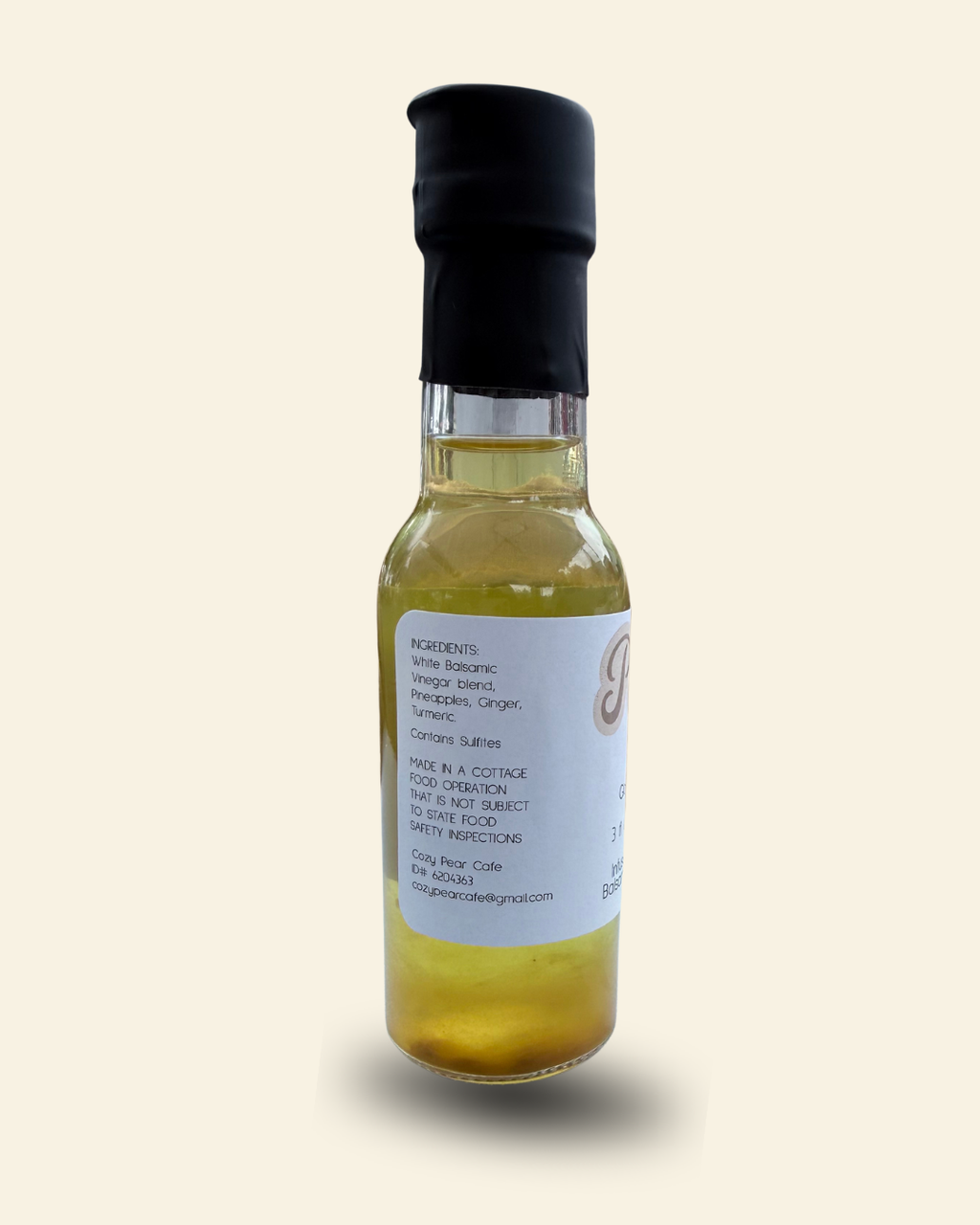 A bottle of Cozy Pear Cafe Glow Tonic, made from distilled white balsamic vinegar, featuring a white label and a black cap, set against a solid cream background.