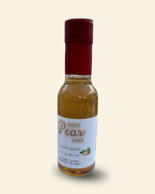 A small glass bottle of Pear Cafe Golden Breeze natural white vinegar with a dark red cap and a white label, set against a solid cream-colored background.