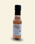 A small glass bottle of Cozy Pear Cafe Nectar & Vine infused white balsamic vinegar, featuring a white label and a black cap, set against a solid cream-colored background.