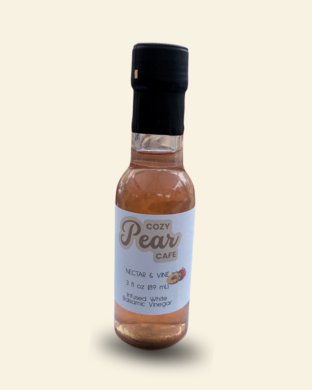 A small glass bottle of Cozy Pear Cafe Nectar & Vine infused white balsamic vinegar, featuring a white label and a black cap, set against a solid cream-colored background.