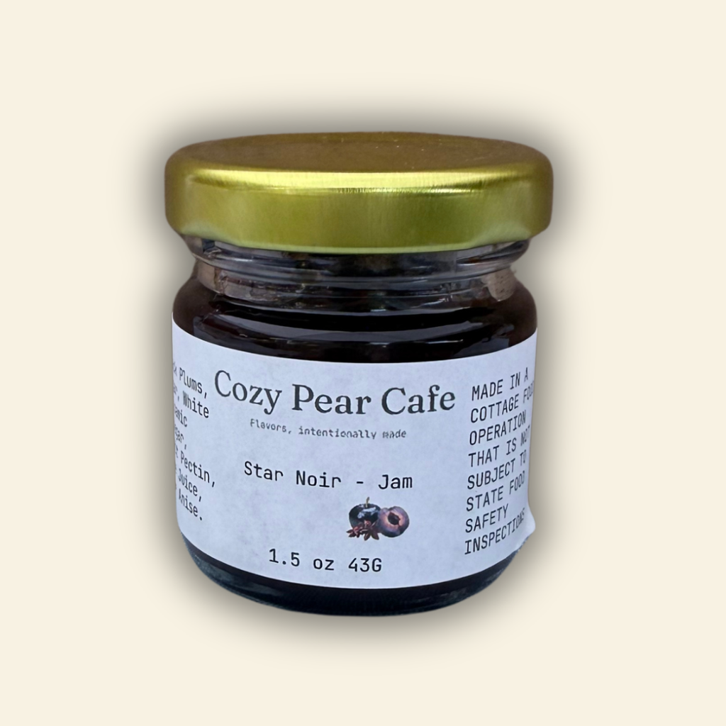 A jar of Cozy Pear Cafe Star Noir - Jam, featuring a white label and a metallic gold lid, set against a solid cream-colored background.
