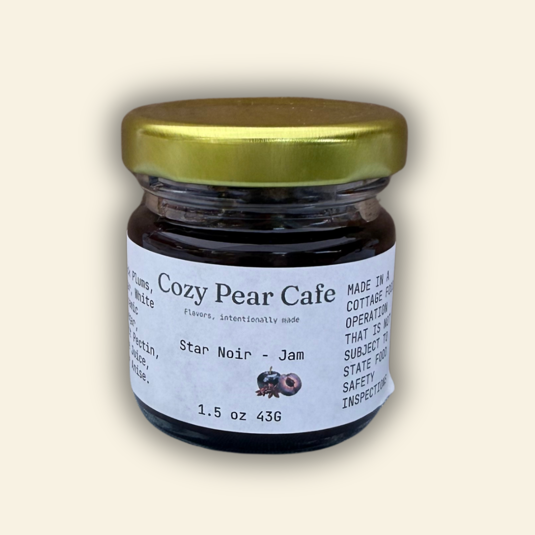 A jar of Cozy Pear Cafe Star Noir - Jam, featuring a white label and a metallic gold lid, set against a solid cream-colored background.