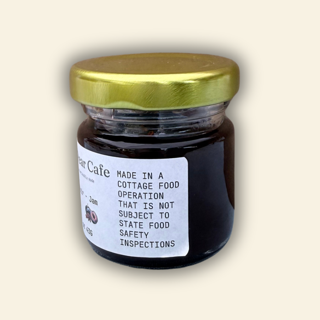 A jar of Cozy Pear Cafe Star Noir - Jam, featuring a white label and a metallic gold lid, set against a solid cream-colored background.