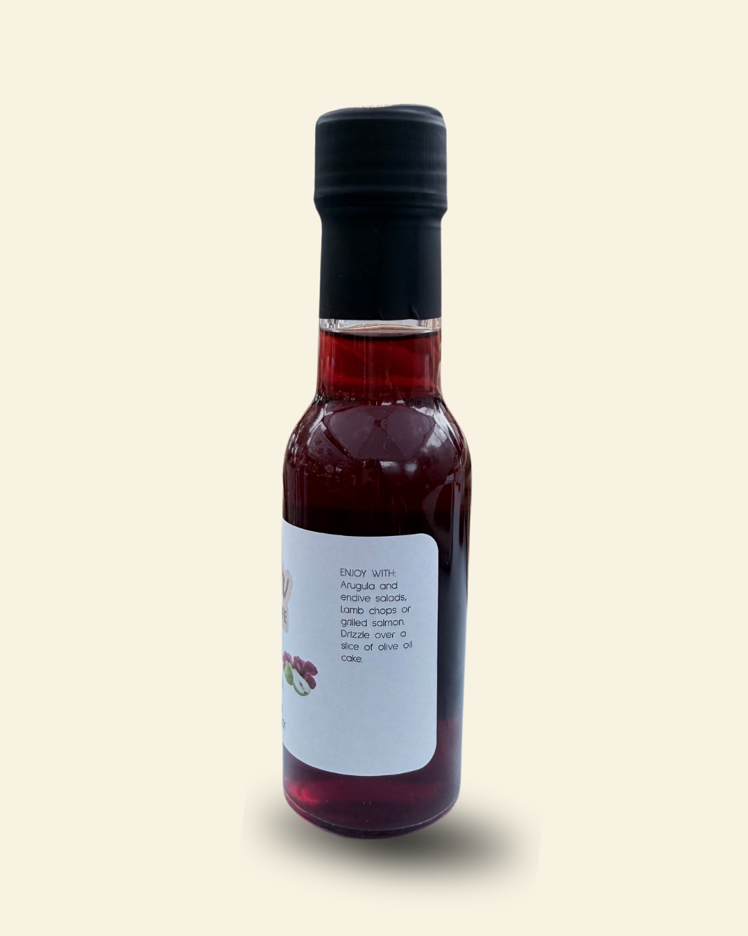 A small glass bottle of Cozy Pear Cafe Velvet Petal infused white balsamic vinegar, featuring a white label and a black cap, set against a solid pale cream background.